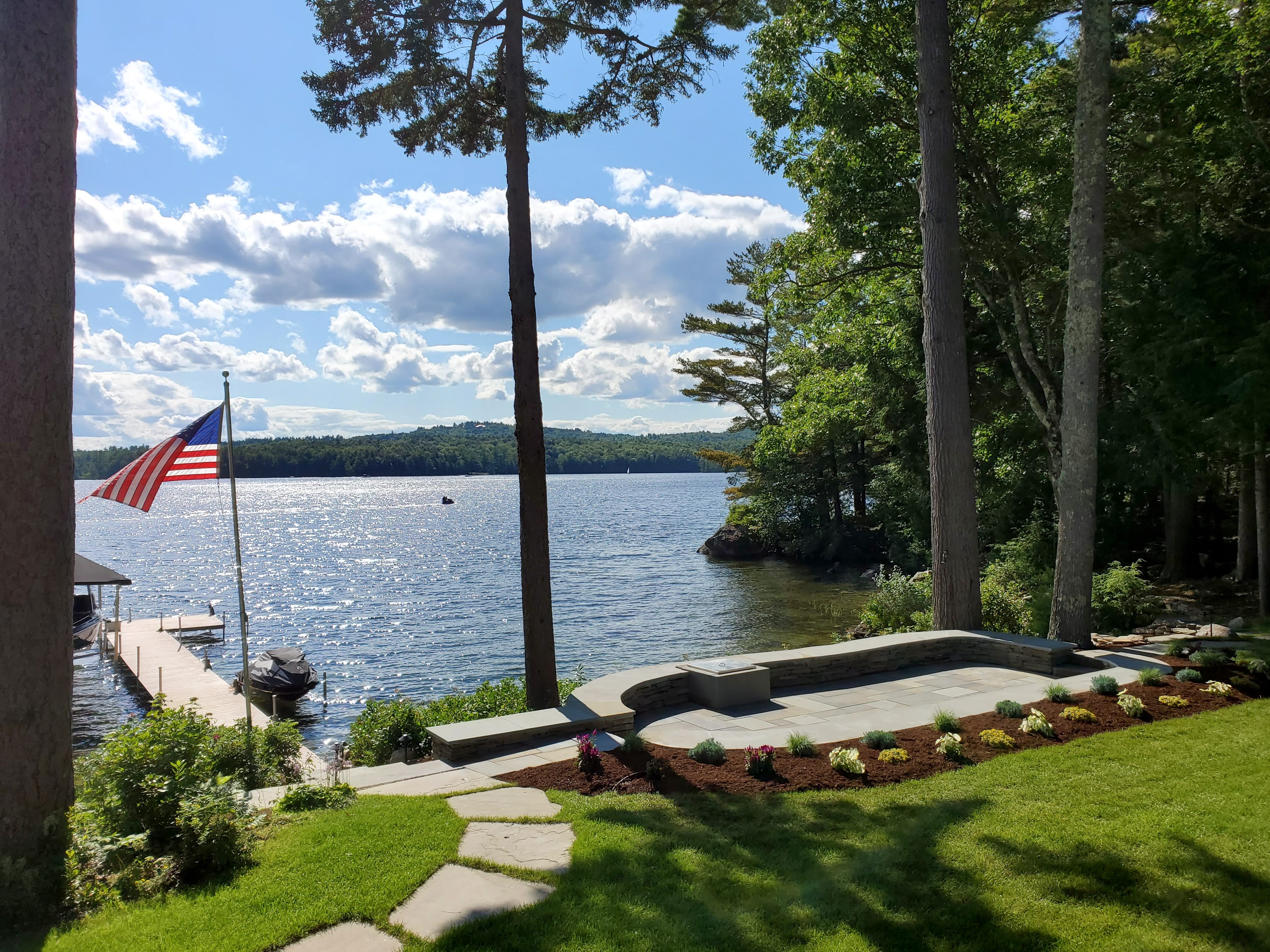 Finished lakefront bluestone patio with American flag, dock, and manicured beds