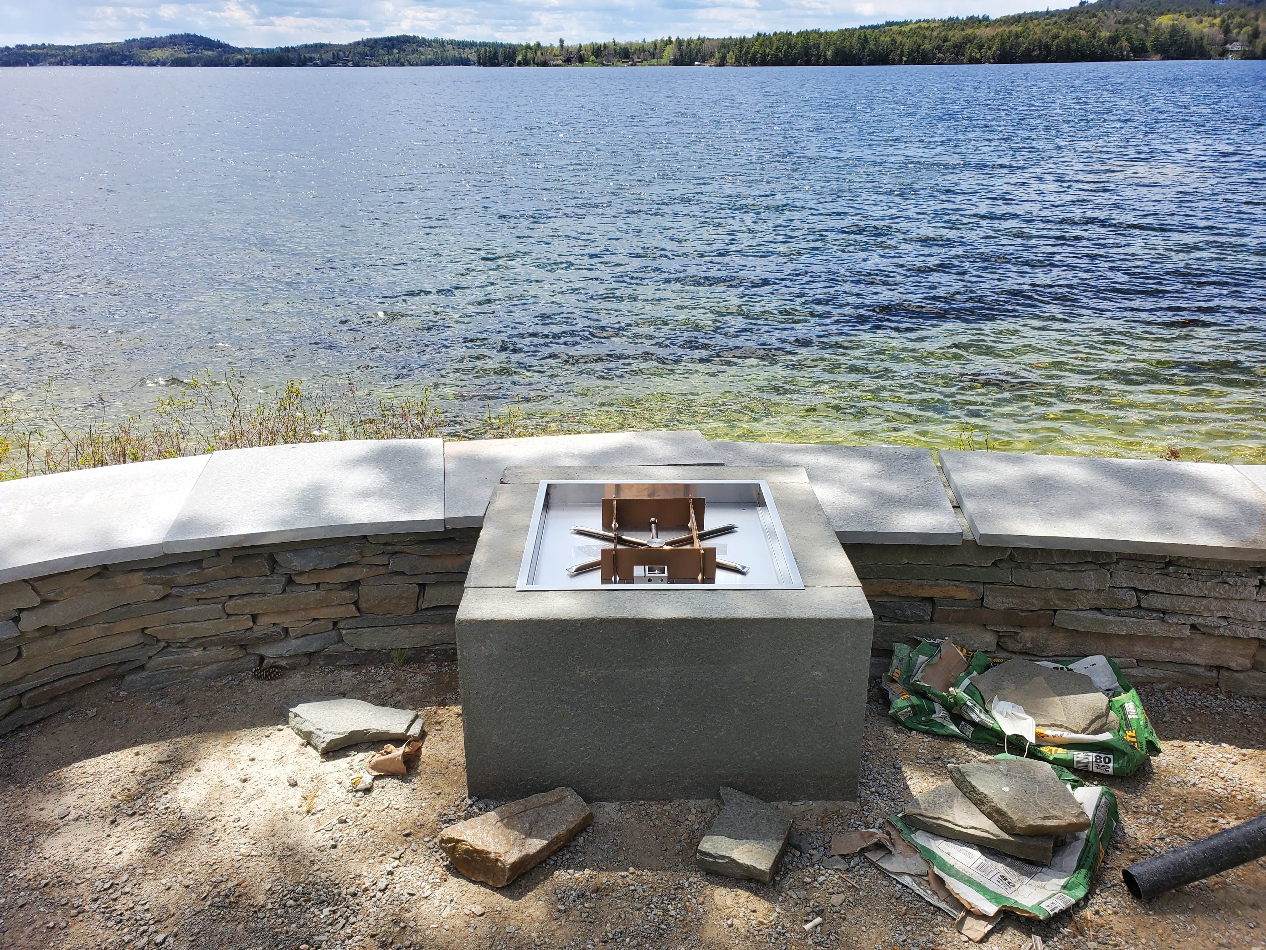 Stainless fire pit set on a stacked stone base at the edge of a lake