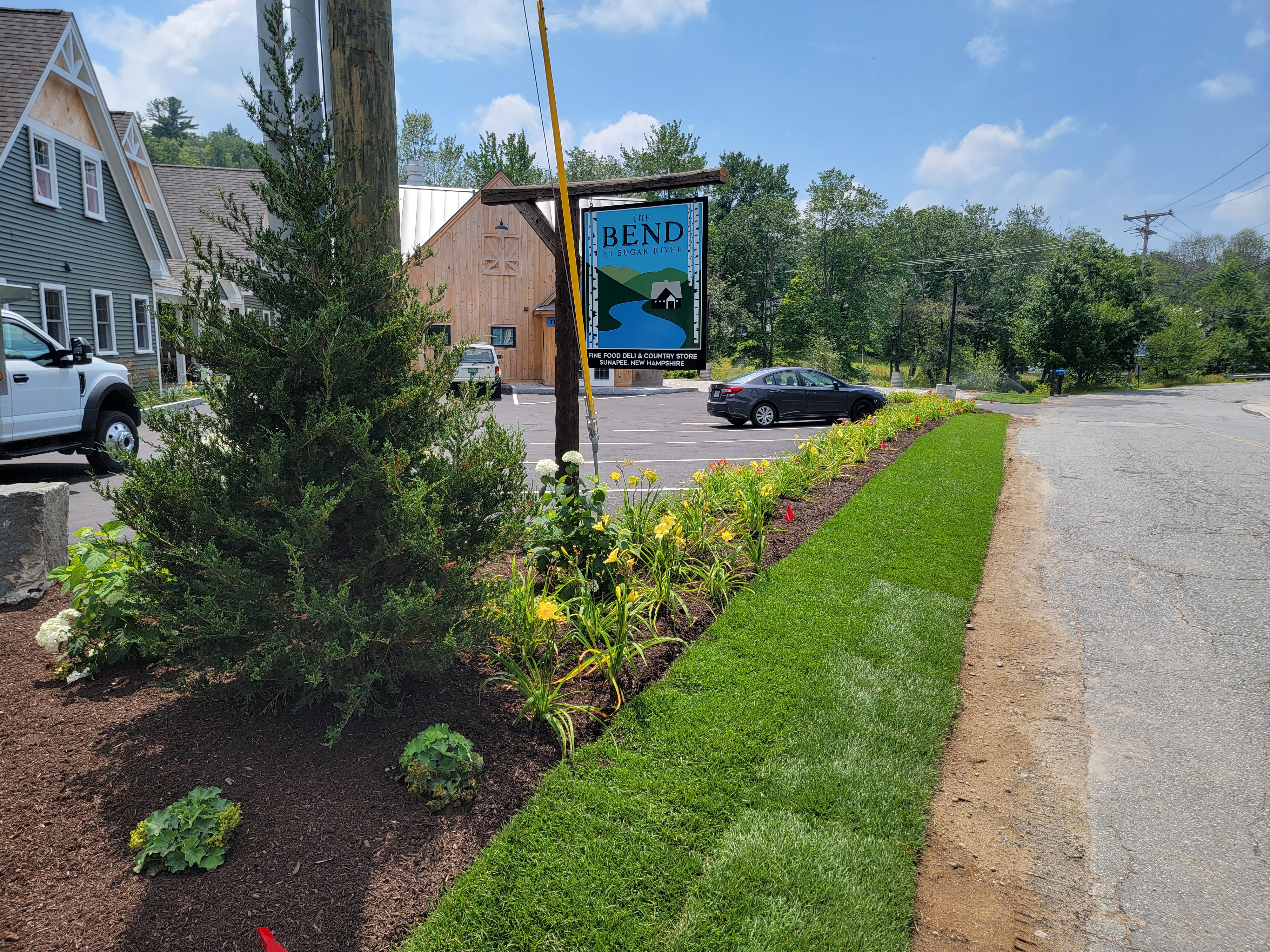 Commercial landscape with fresh sod ribbon and a mulched perennial bed along a business sign
