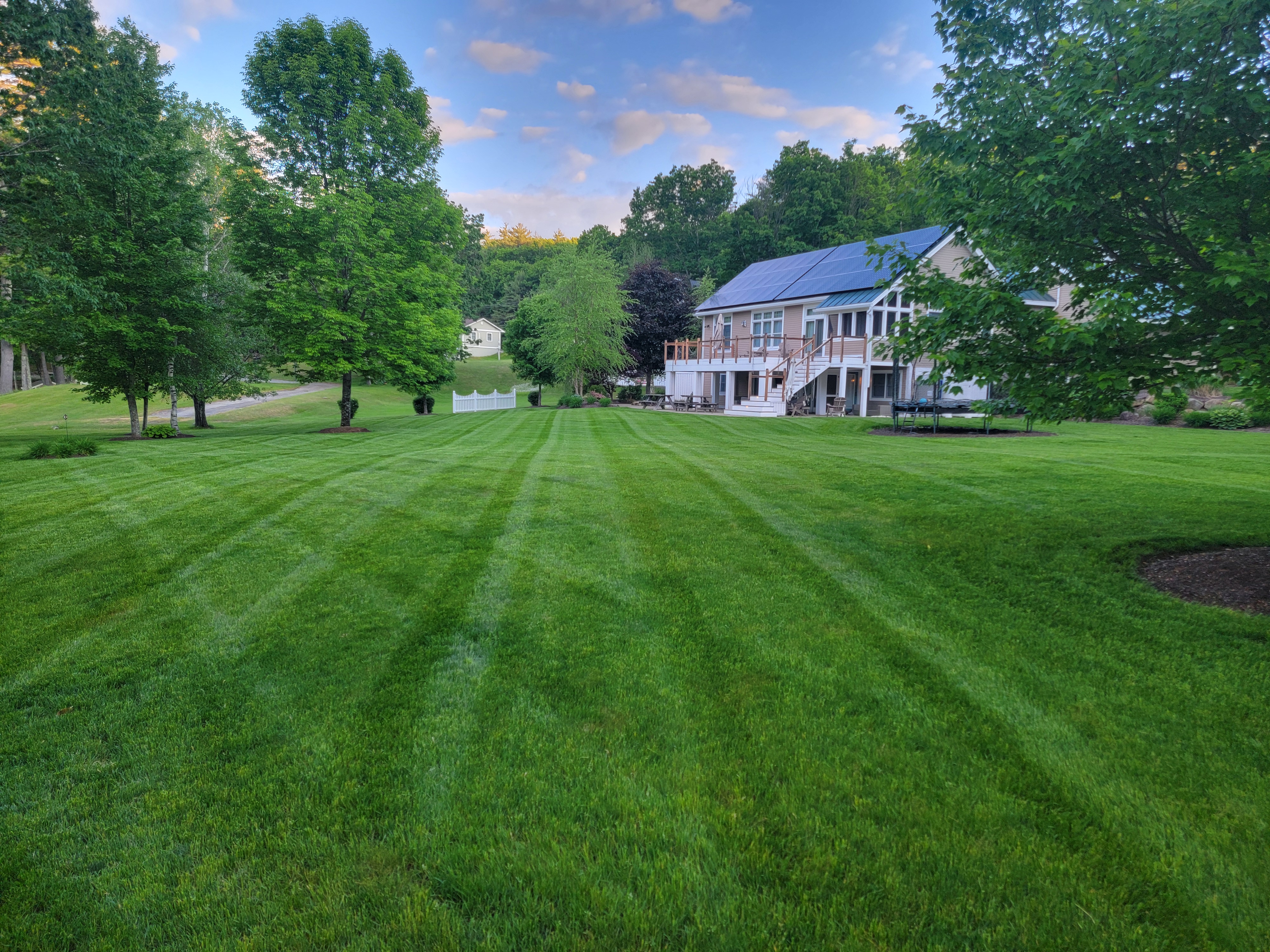 Golden-hour shot of a perfectly striped backyard lawn rolling toward a deck-front home