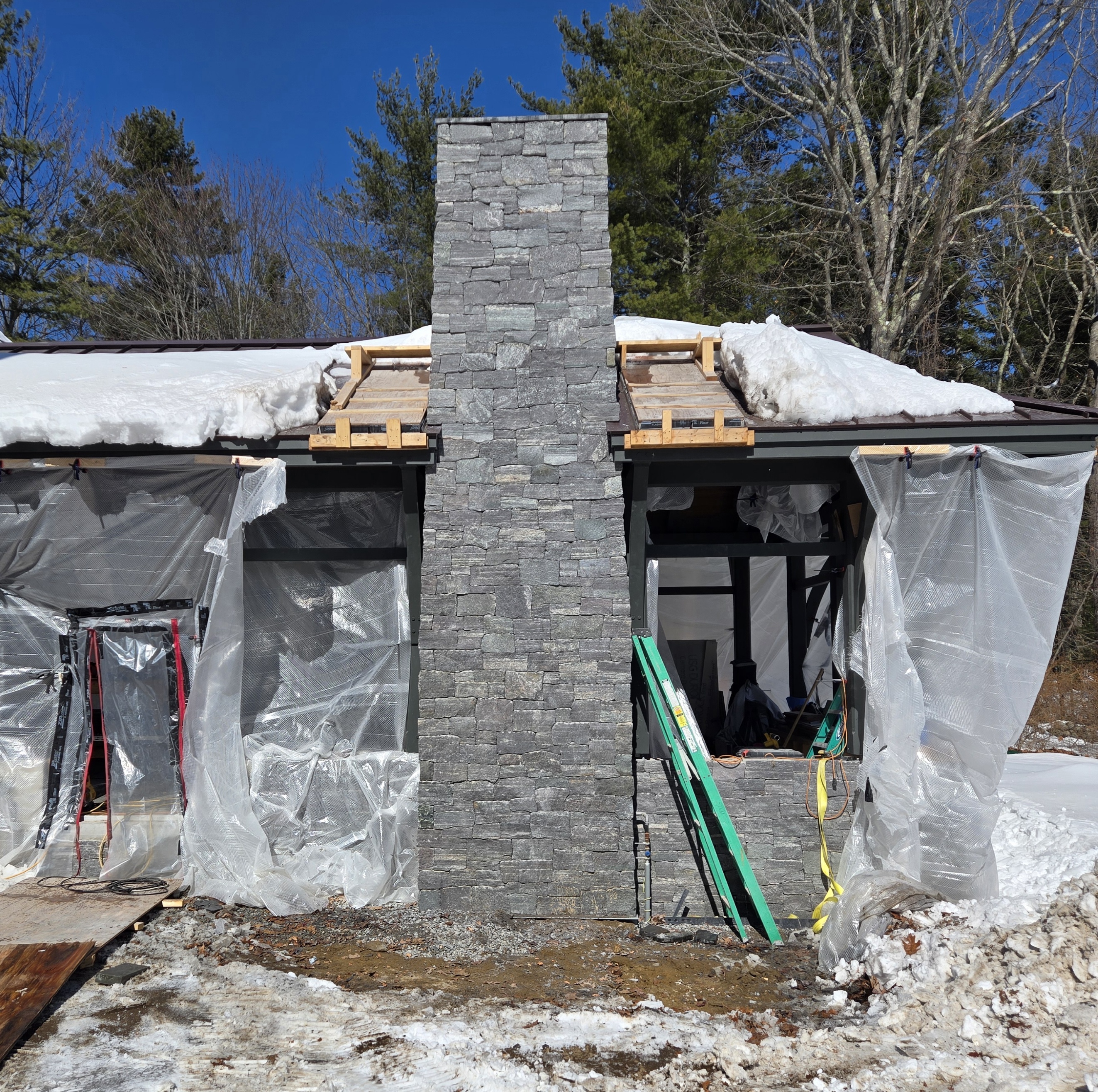 New stacked-stone chimney rising out of a home under construction