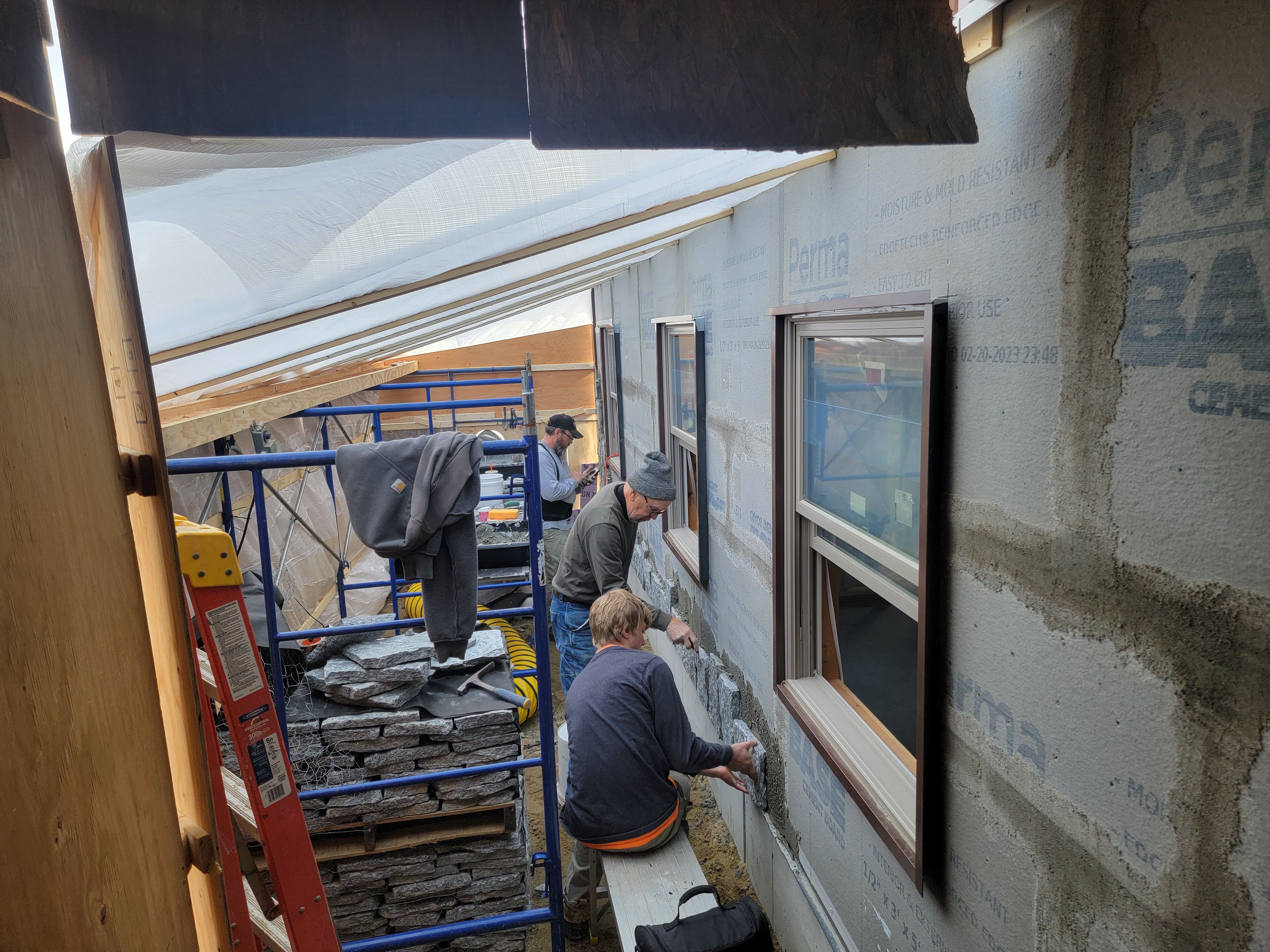 Masons installing veneer stone on a wrapped house wall