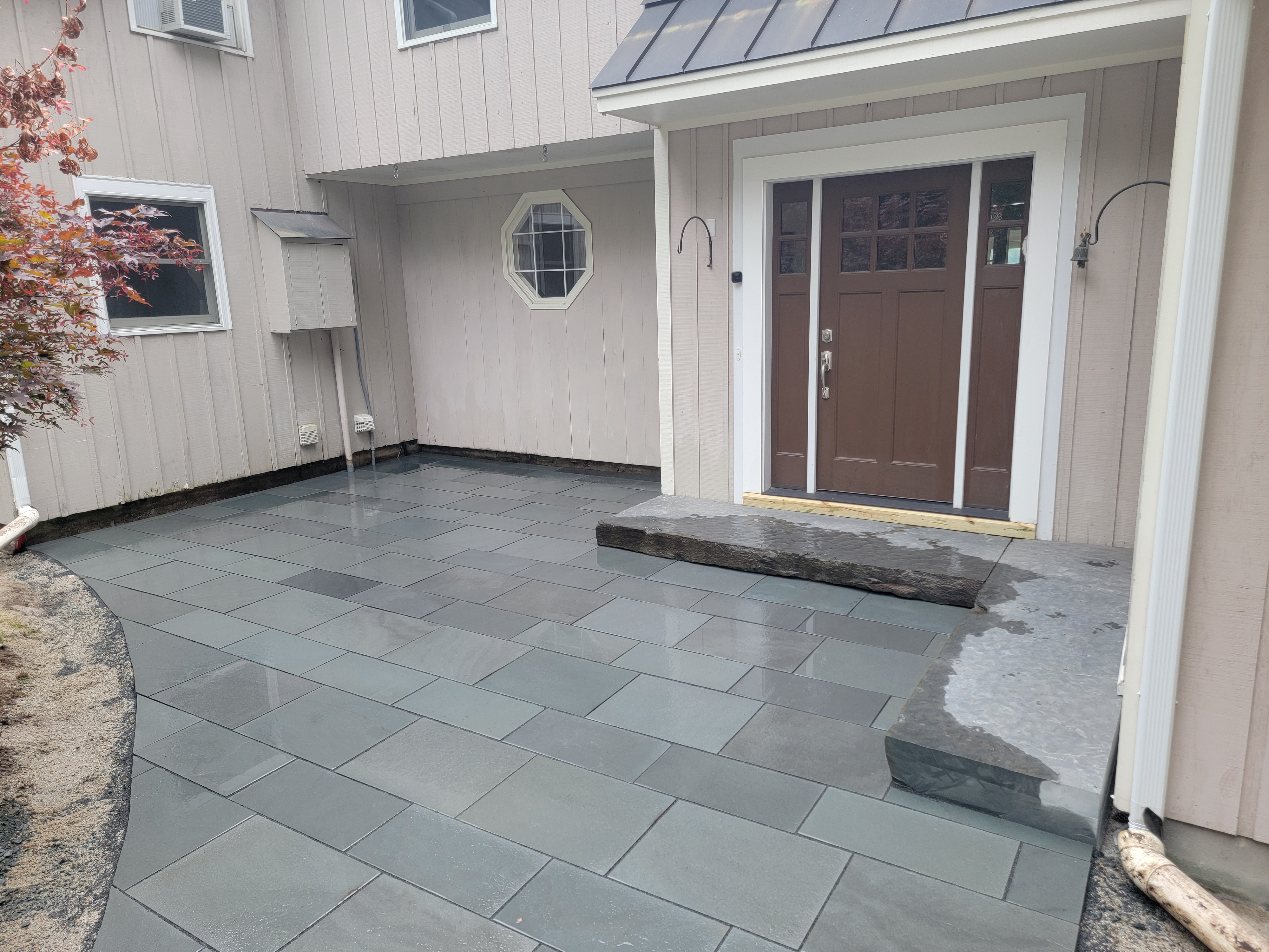 Wet bluestone landing at a covered front entry with Japanese maple
