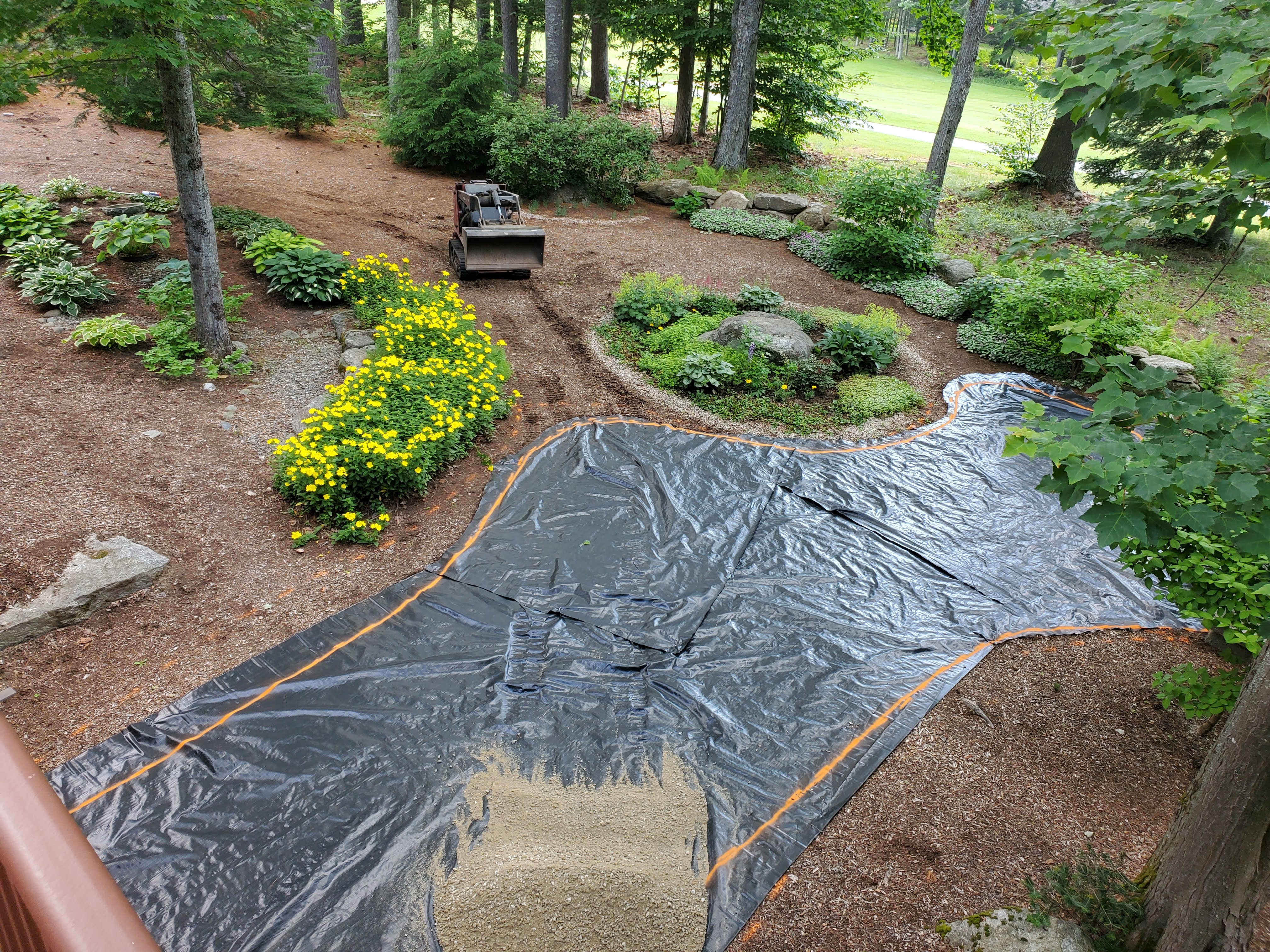 Backyard prep with black tarp covering subbase before patio install