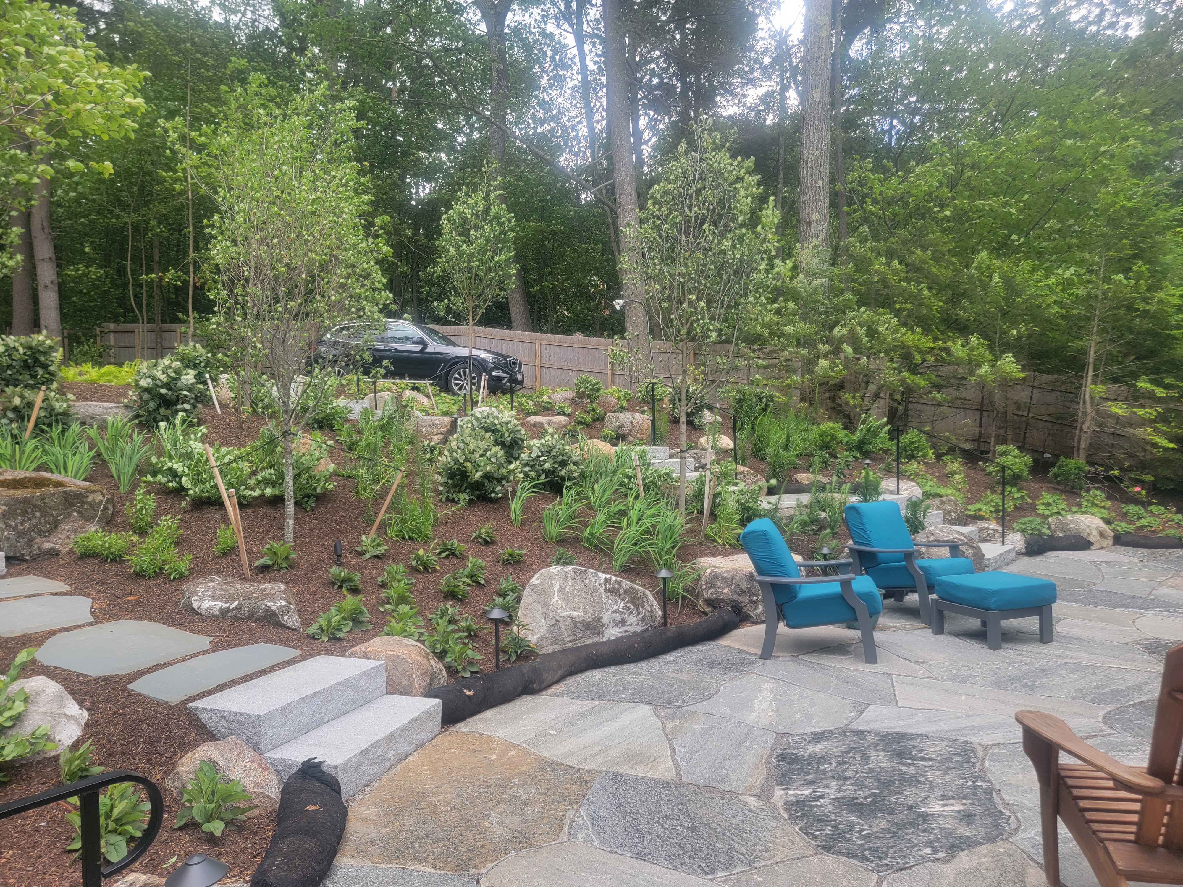 Mixed flagstone patio with blue Adirondack chairs and new plantings