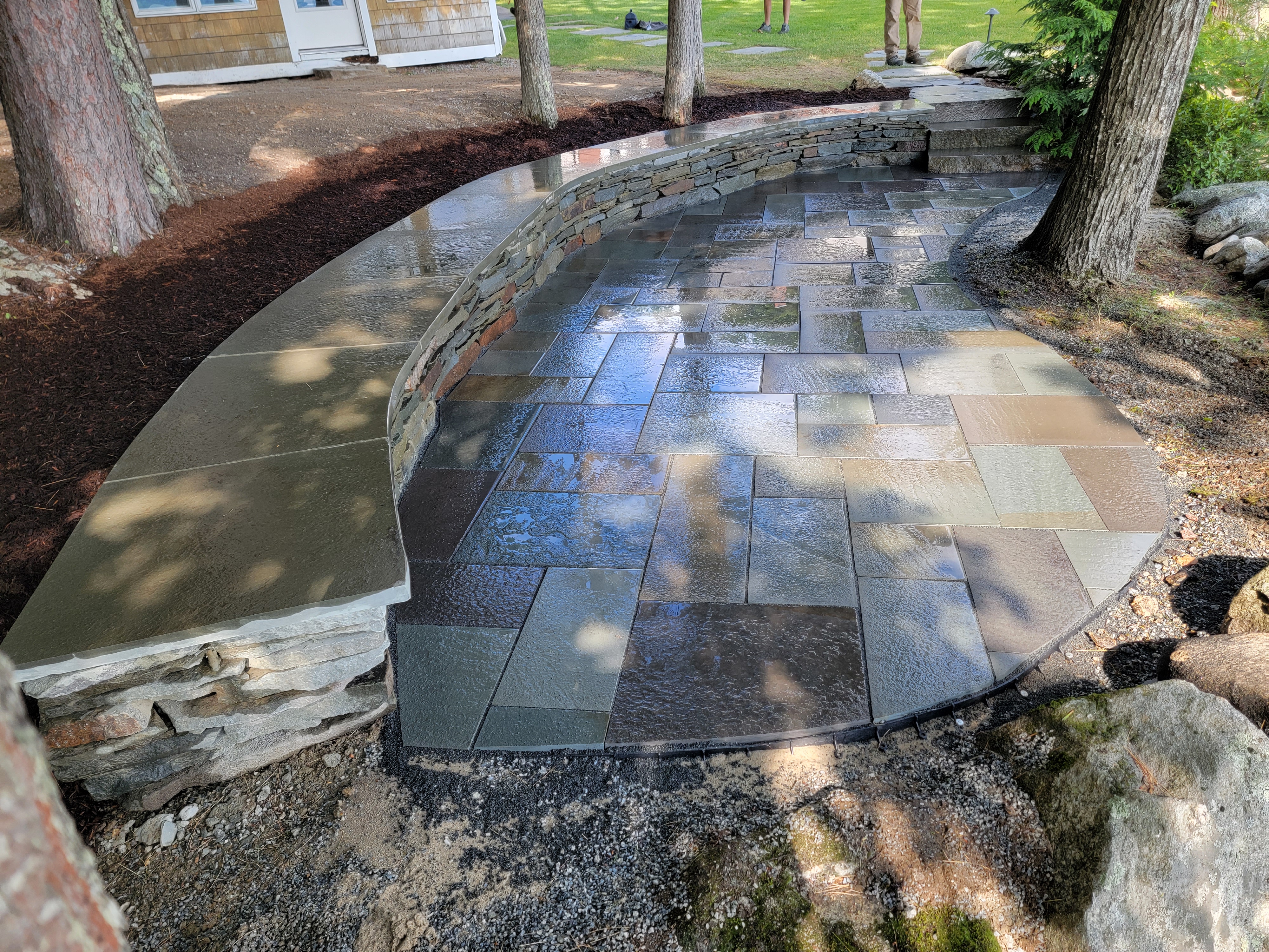 Two-tier bluestone patio with stacked-stone retaining wall after rain
