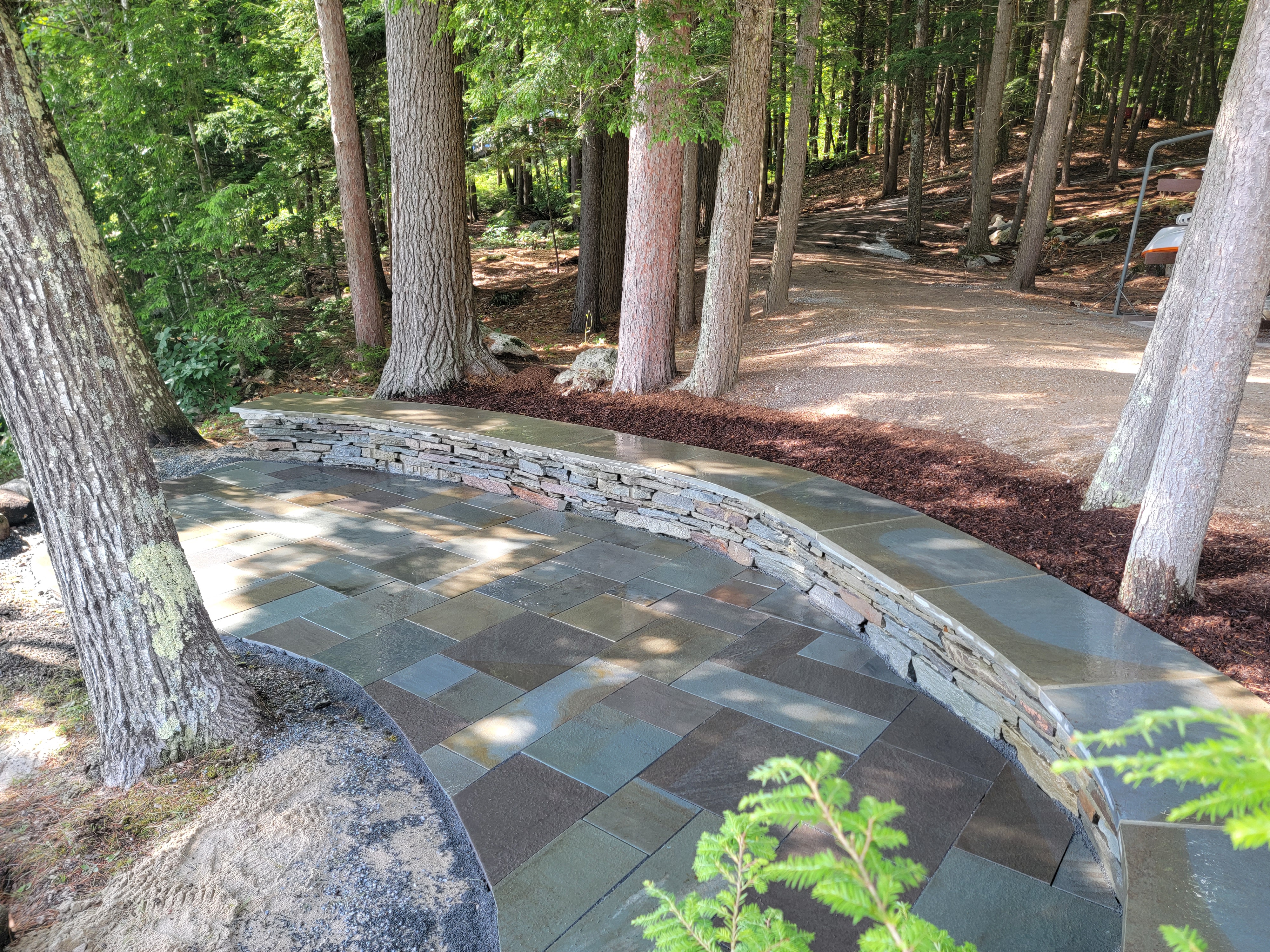 Bluestone patio with curved stacked-stone wall in a mature wooded setting