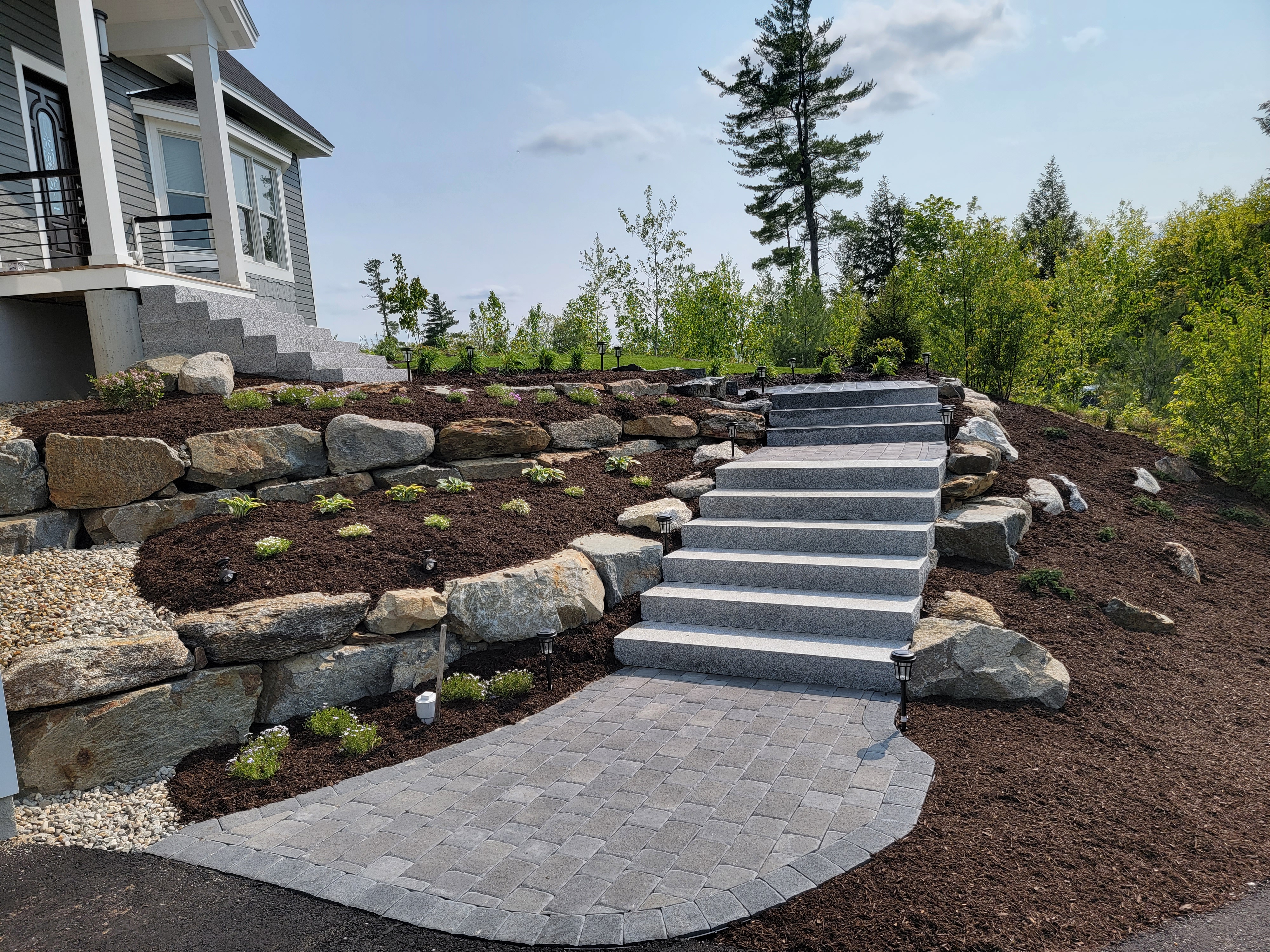 Wide granite-block staircase ascending through new plantings