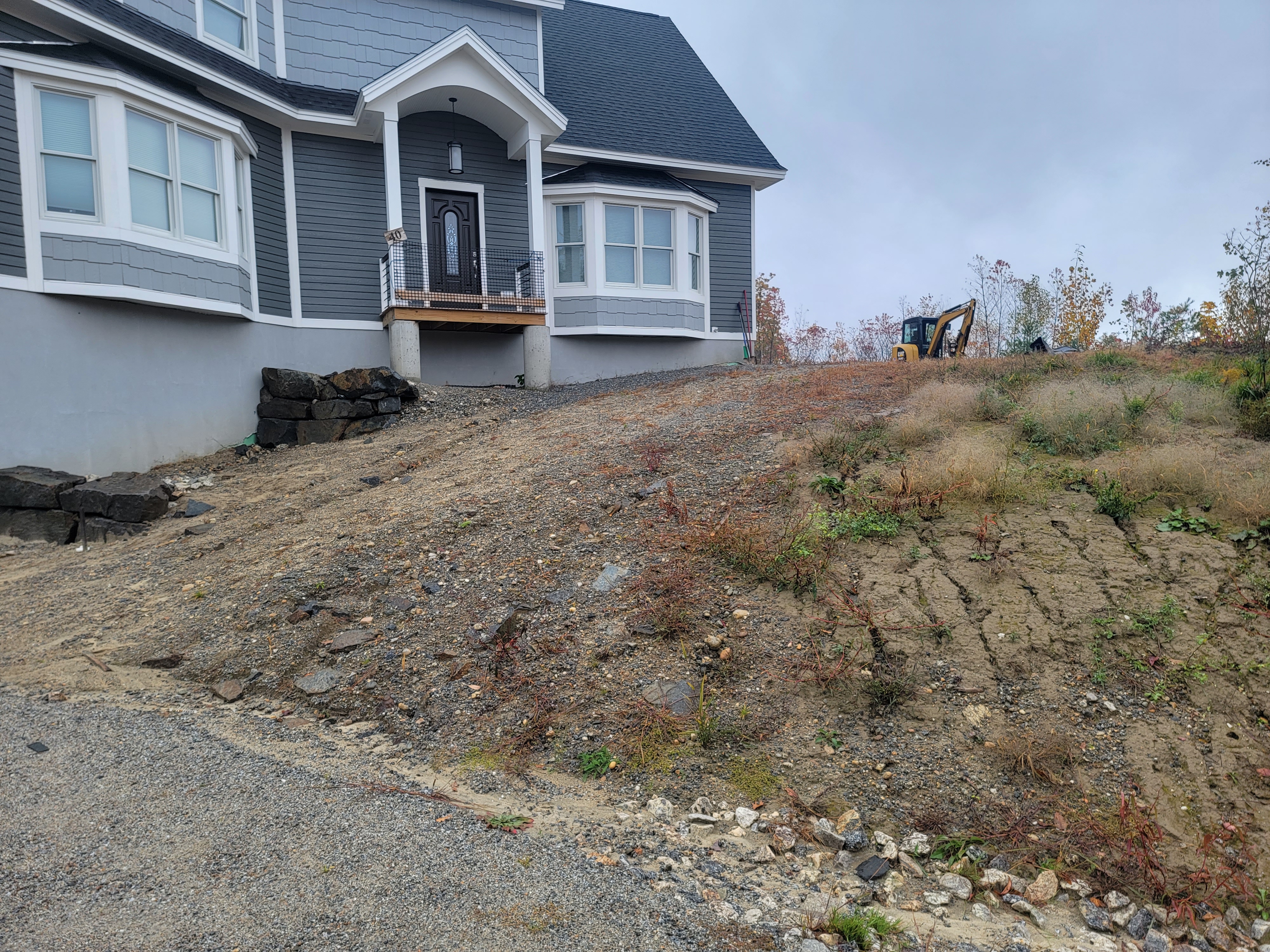 Bare dirt slope at a navy-clapboard home before stair install