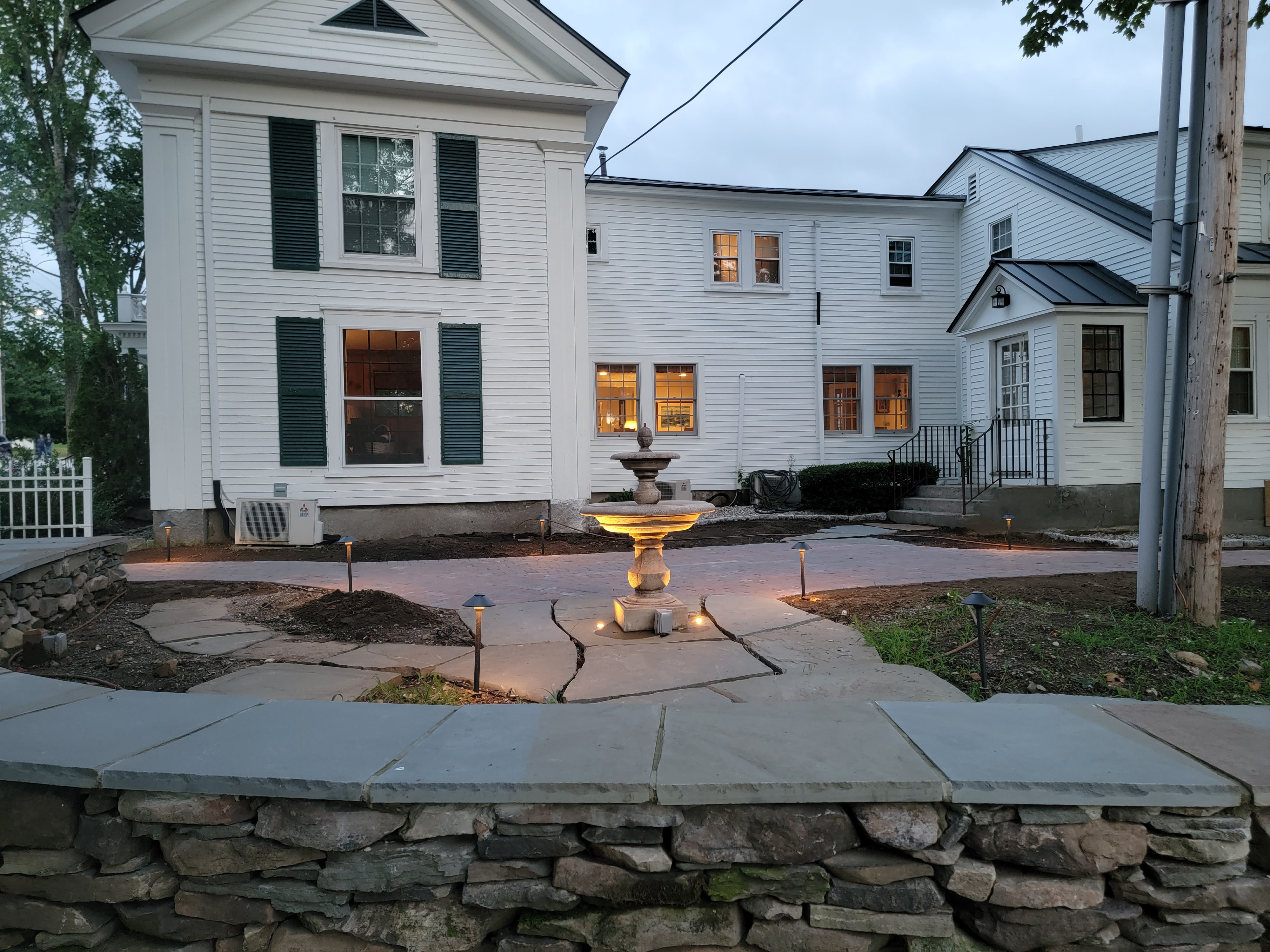 Historic white home at twilight with stone seat wall, fountain, and lit paver walkway