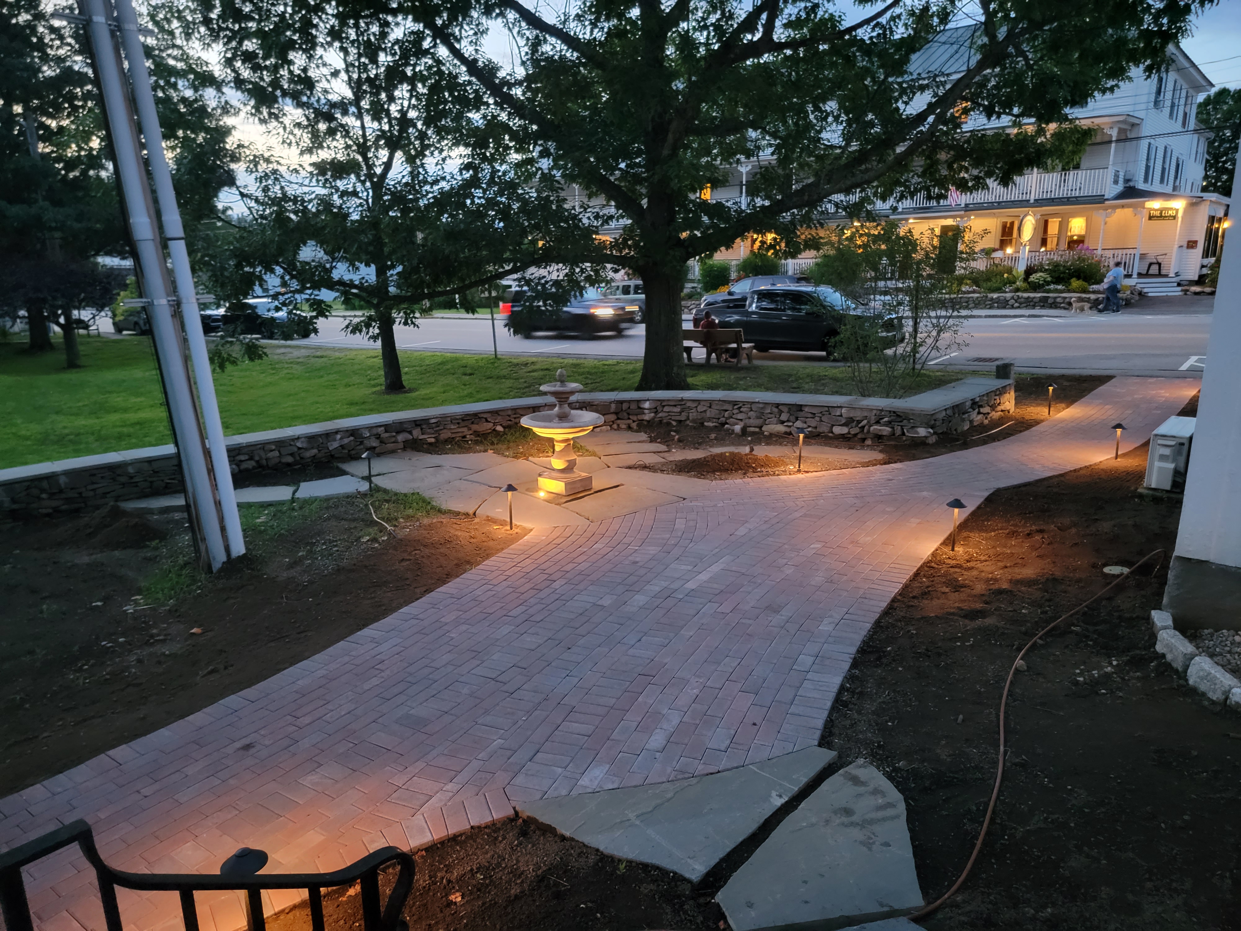 Brick paver walkway with central fountain at twilight, illuminated by path lights
