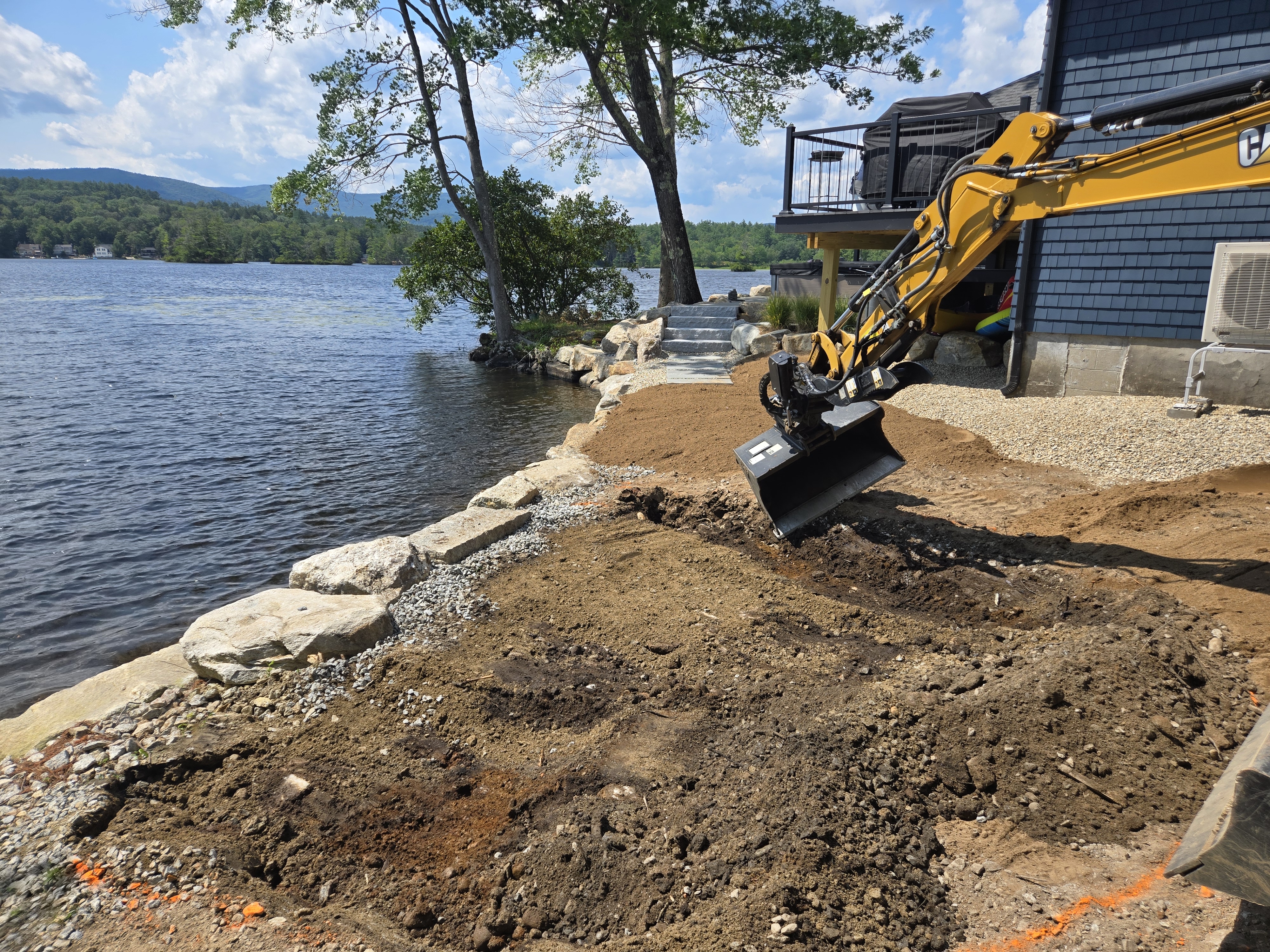 Yellow Cat mini-excavator working a lakefront site with mountains in the background