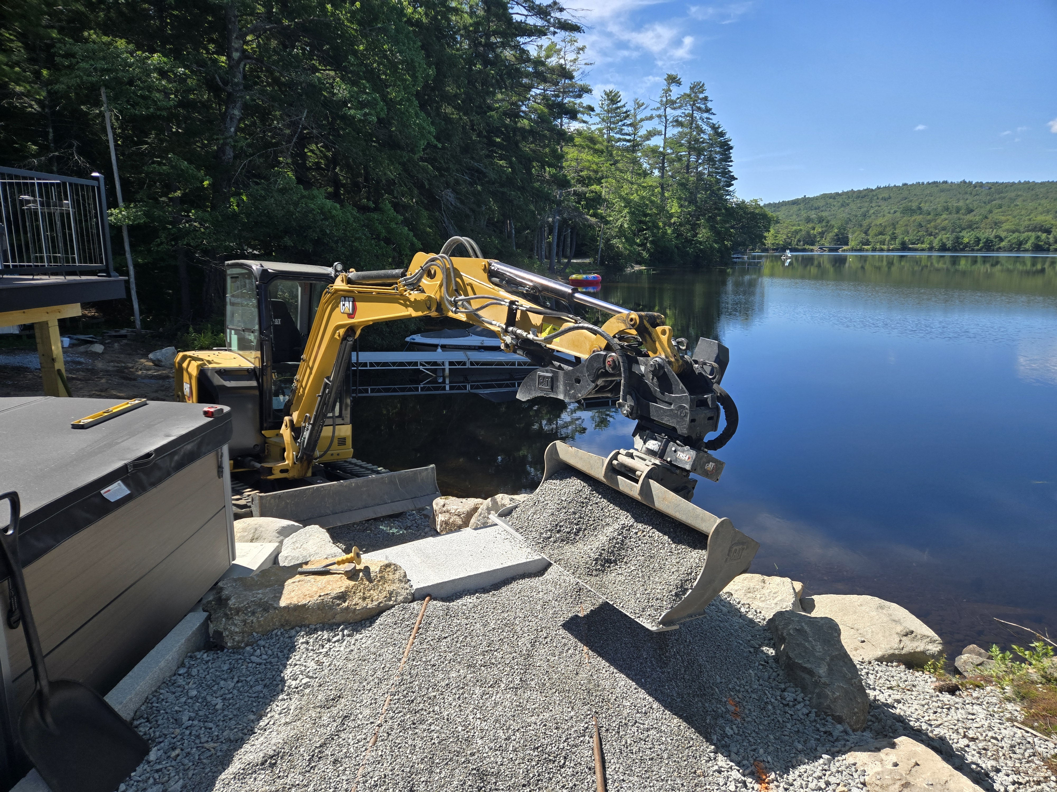 Mini-excavator dropping gravel at the edge of a lake with mountains
