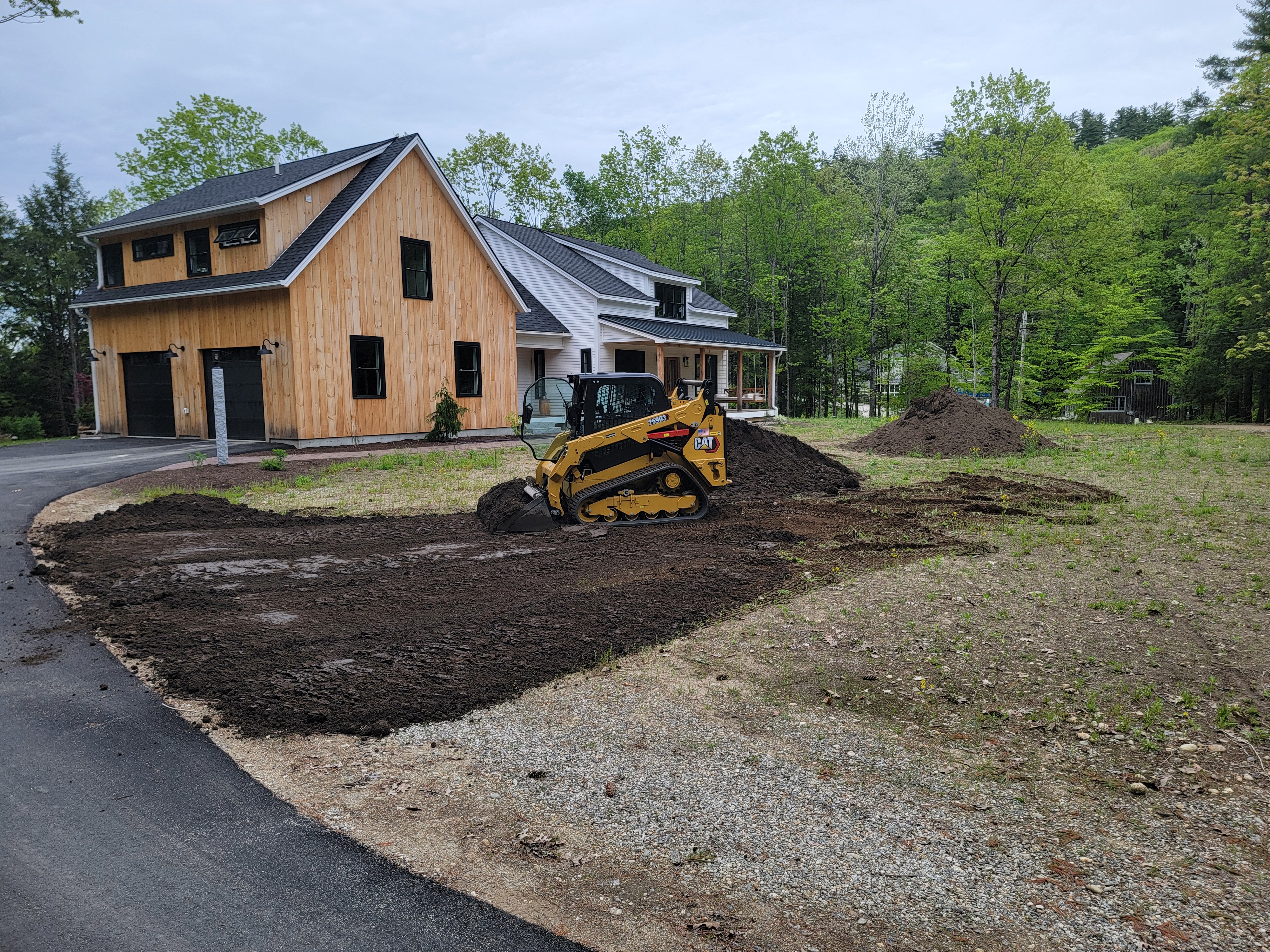 Compact track loader spreading topsoil along the front of a barn-style home